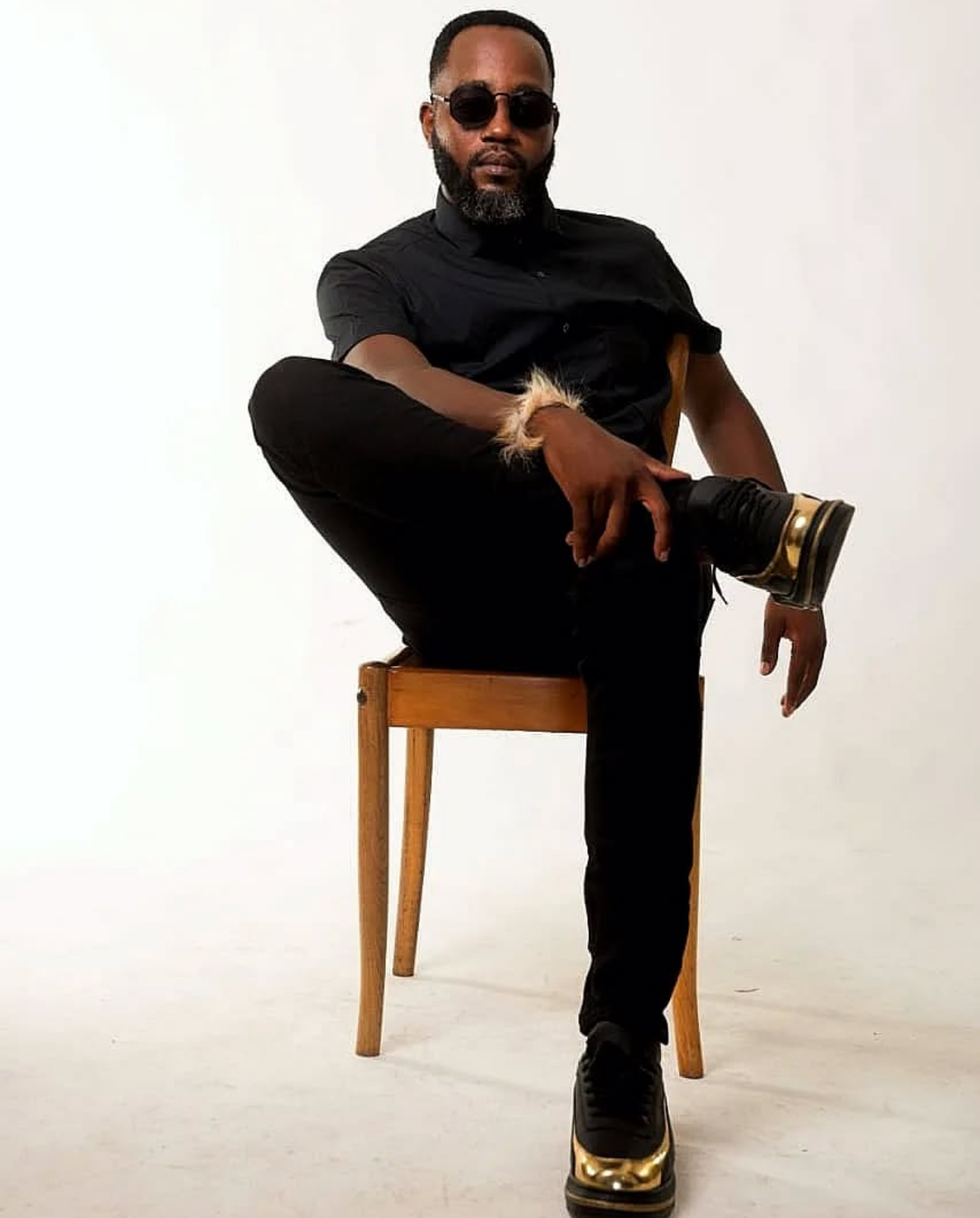 Menzi Biyela seated on a wooden chair in all black with sunglasses