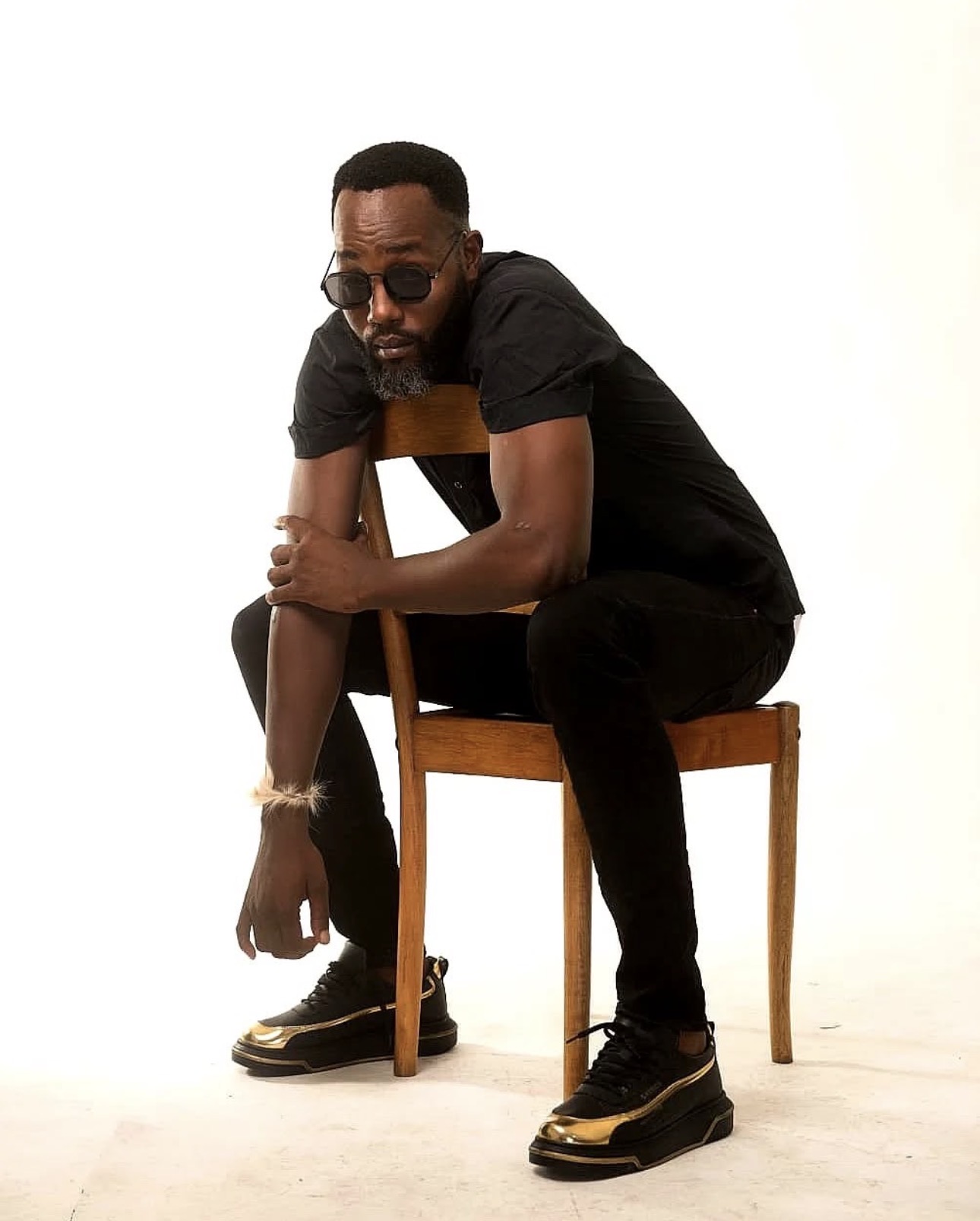Menzi Biyela seated on a wooden chair in an all-black studio shoot