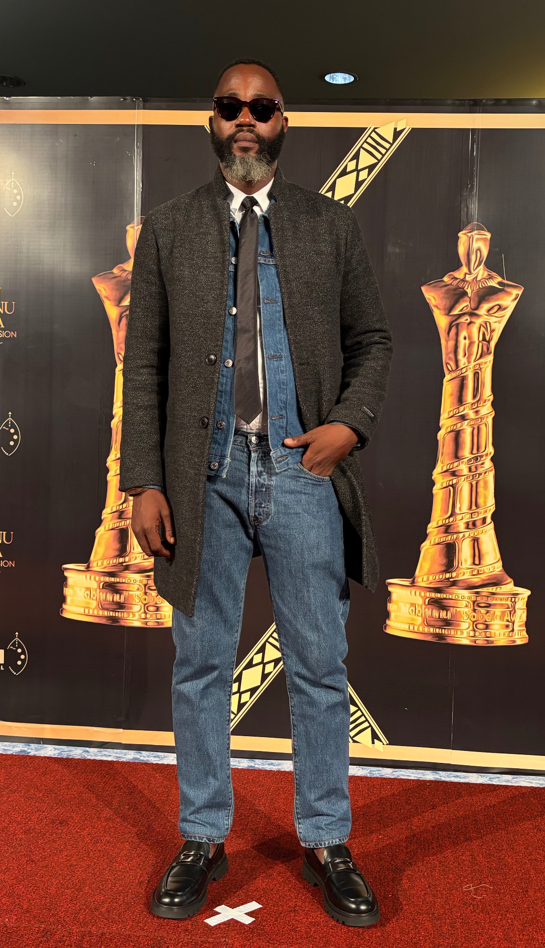 Menzi Biyela on the red carpet in denim and a grey coat at the Simon Mabhunu Sabela Awards